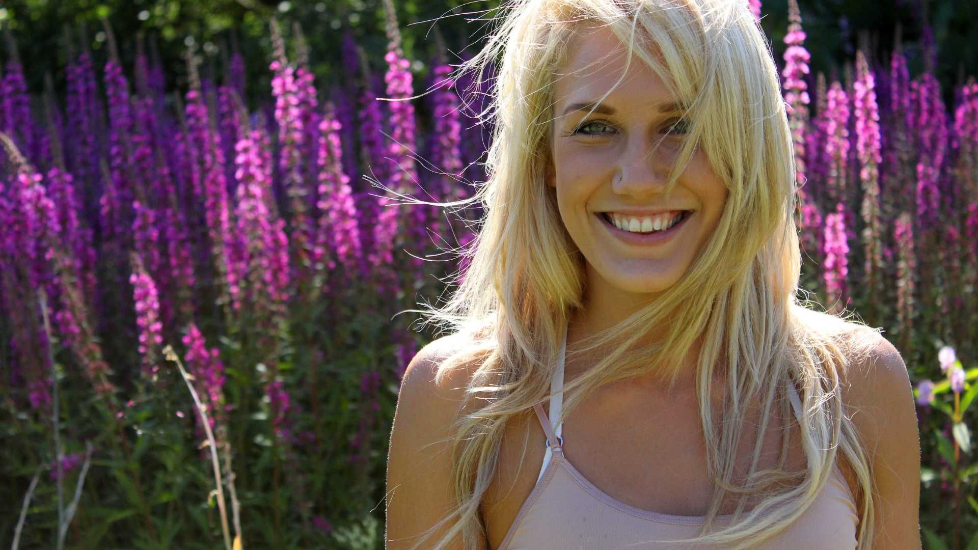A woman is smiling in front of purple flowers.