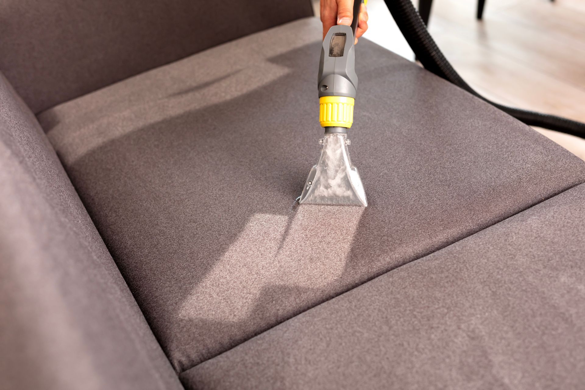 Person using a upholstery cleaner on a gray sofa cushion, removing dirt and stains.