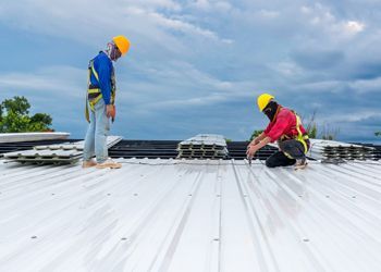 two construction workers are working on a metal roof .