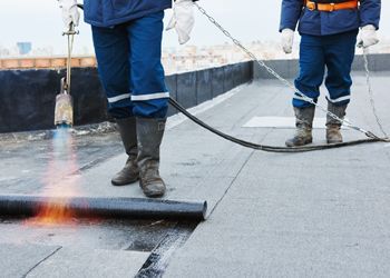 two men are working on a roof with a torch .