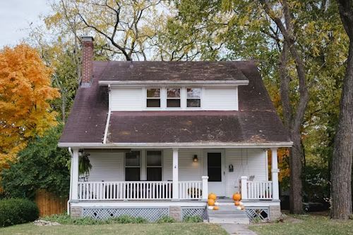A white house with a brown roof and a porch decorated for halloween.