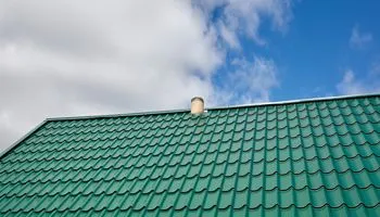 A green roof with a chimney on top of it and a blue sky in the background.