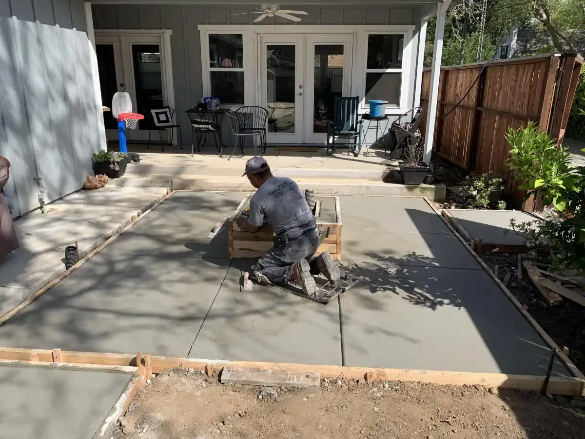 A man is working on a concrete patio in front of a house.