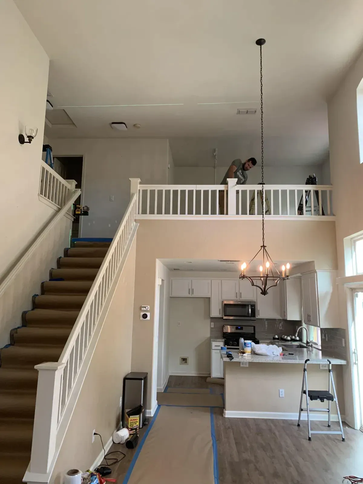 A man is standing on a ladder in a living room next to a staircase.