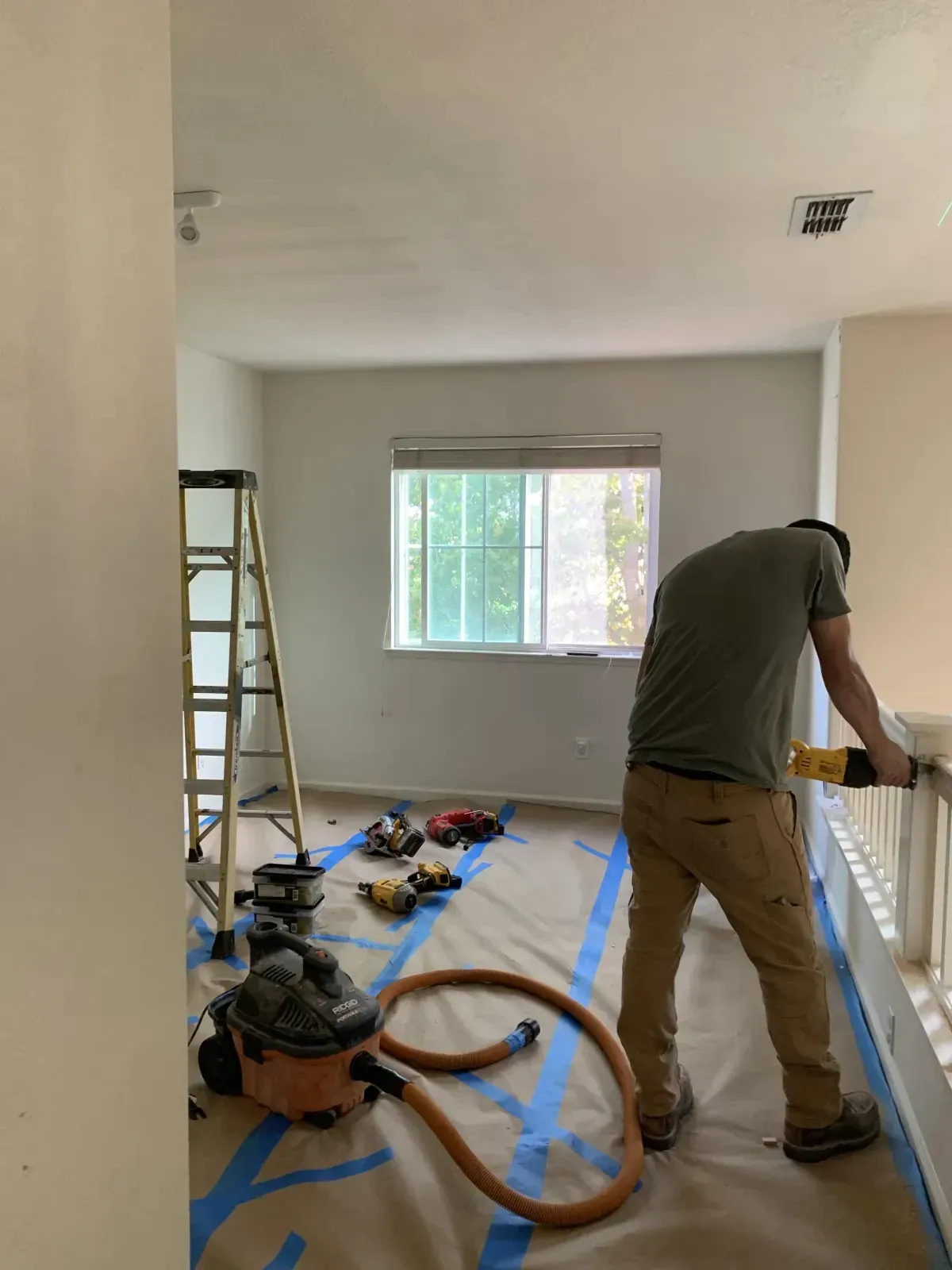 A man is standing in a room with a ladder and a vacuum cleaner.