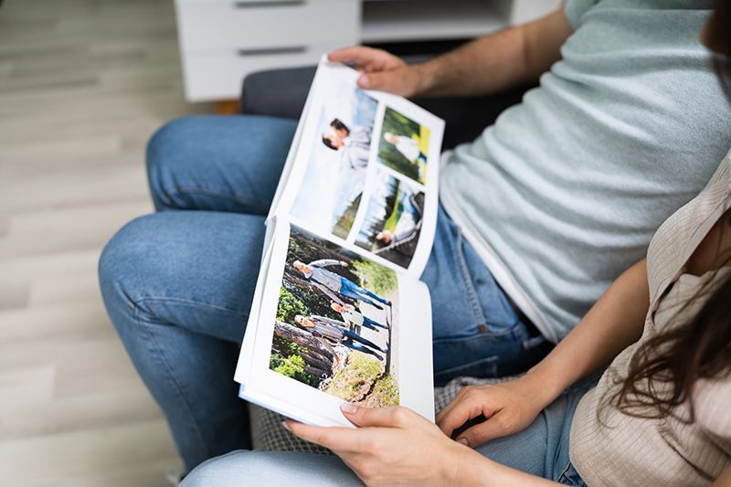 Two people sit side-by-side, holding and looking through an open photo album filled with pictures of their outdoor travels.