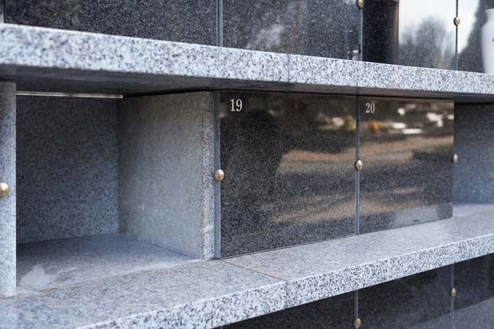Rows of granite columbarium niches, some empty and some sealed with black stone plaques numbered 19 and 20.