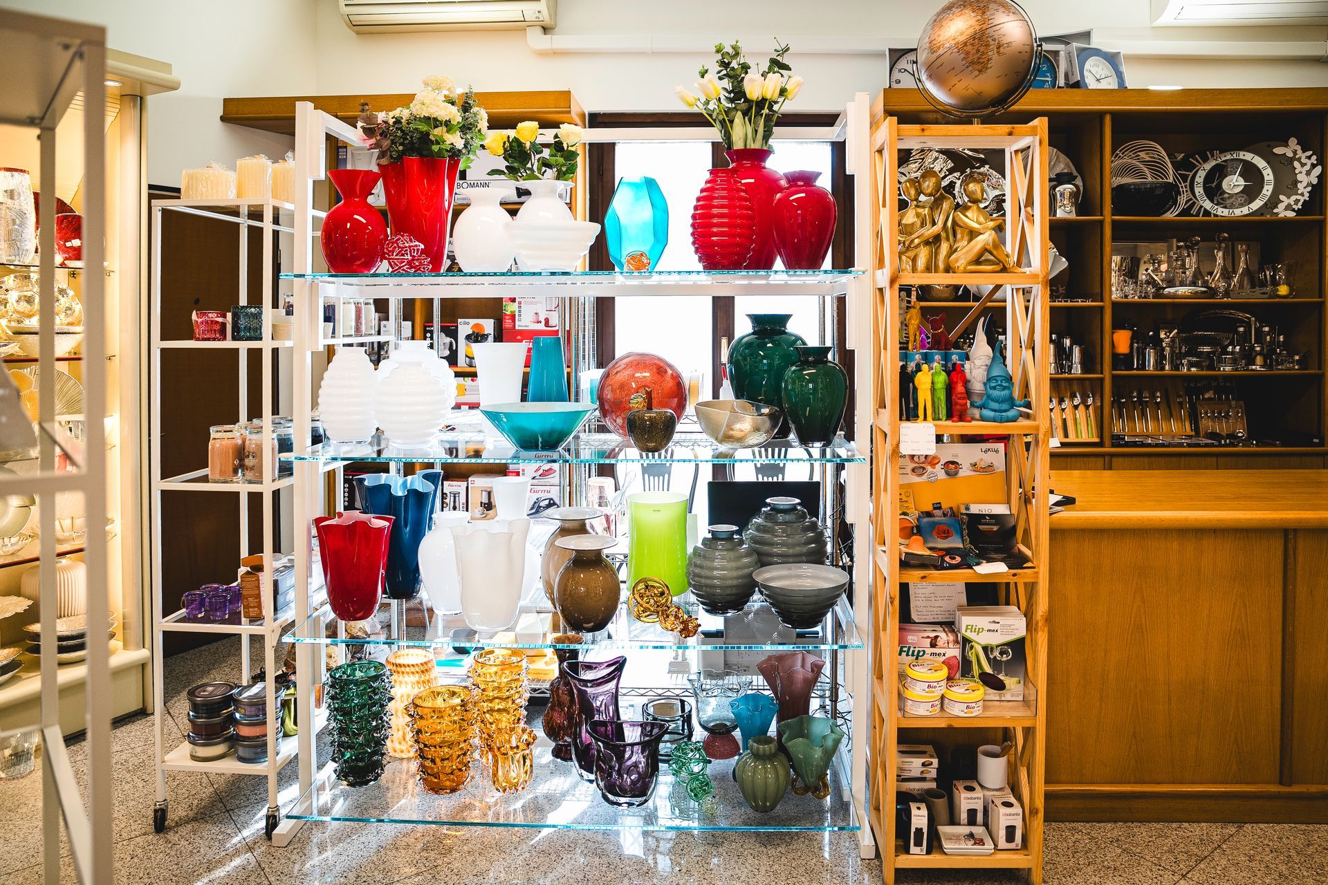 All'interno di un negozio, scaffali pieni di vasi e ornamenti decorativi in ​​vetro di vari colori.