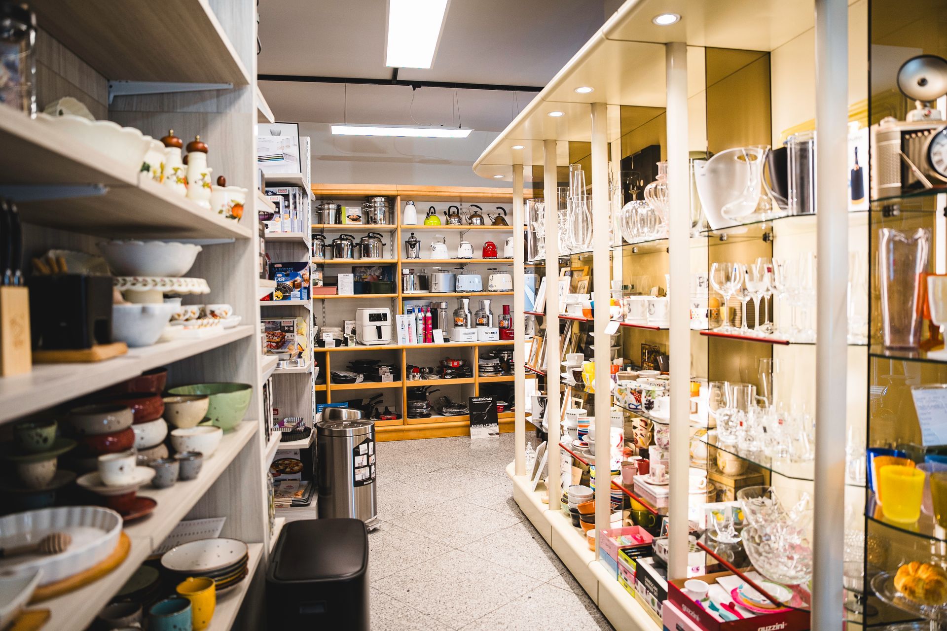 Un corridoio di un negozio di articoli per la casa, pieno di scaffali con utensili da cucina, vetreria e oggetti decorativi.