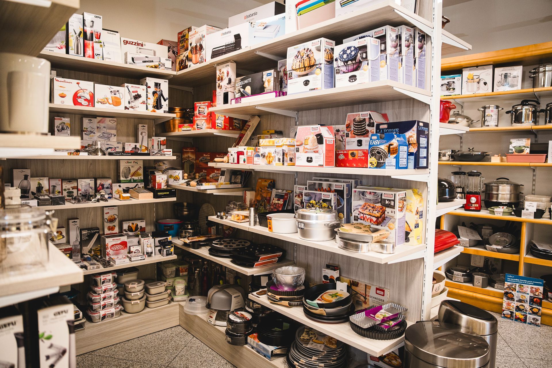 Scaffali pieni di vari elettrodomestici, utensili da cucina e accessori per cucinare in un negozio al dettaglio.