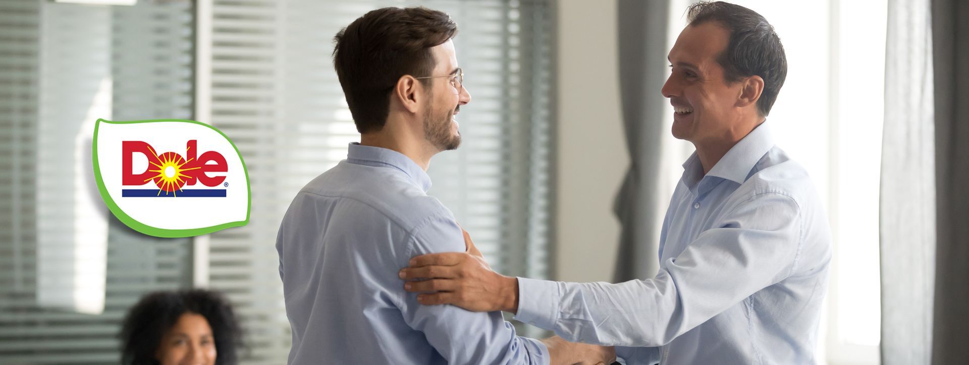 Two men are shaking hands in an office with a dole logo in the background.