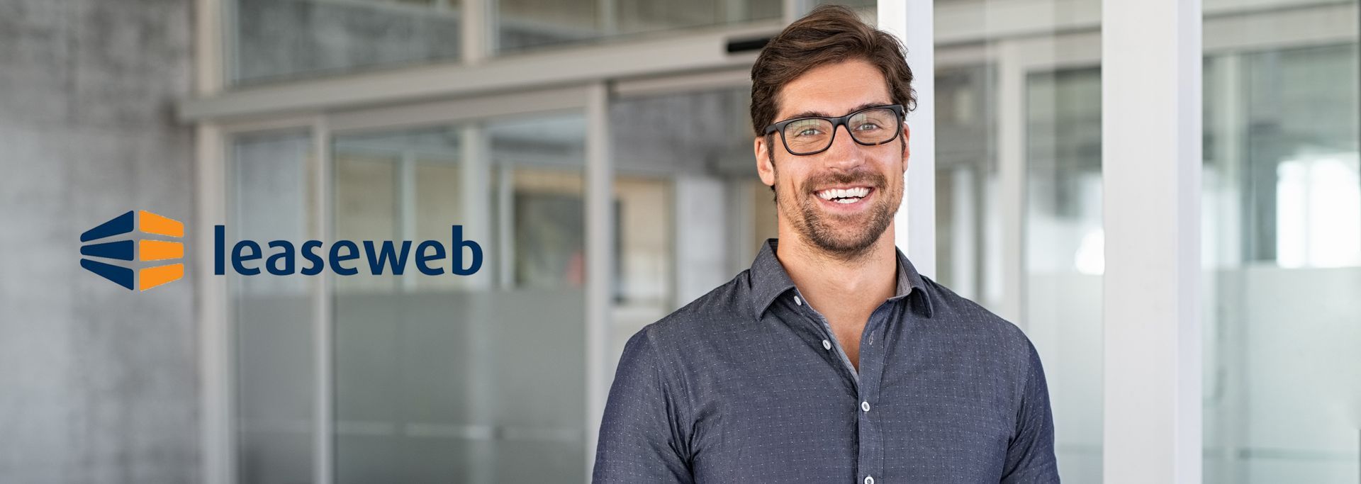 A man wearing glasses is smiling in front of a glass door.