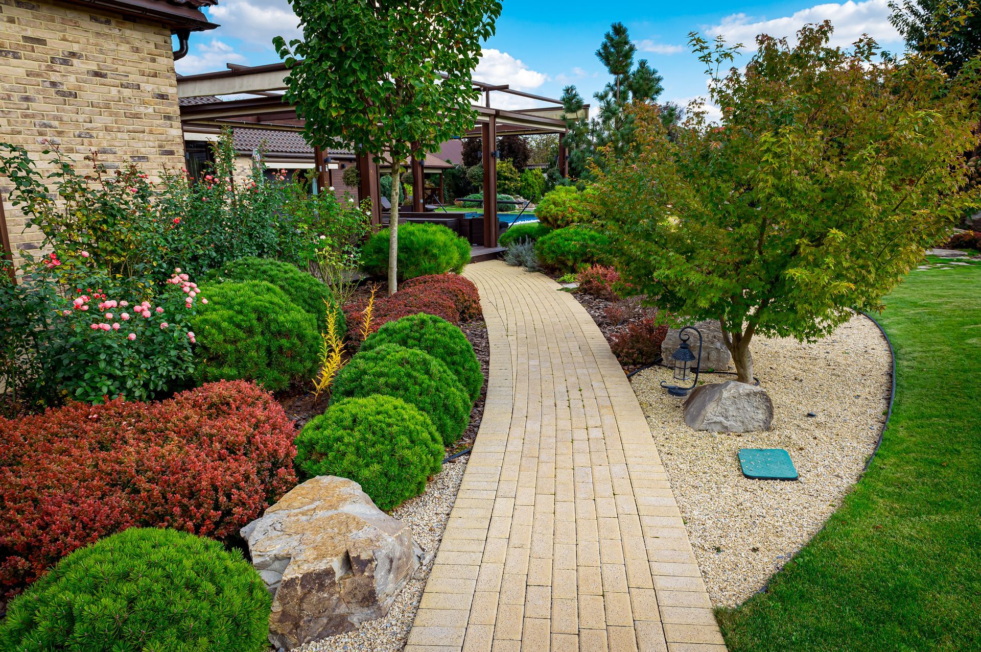 A brick walkway leading to a house in a lush green garden.