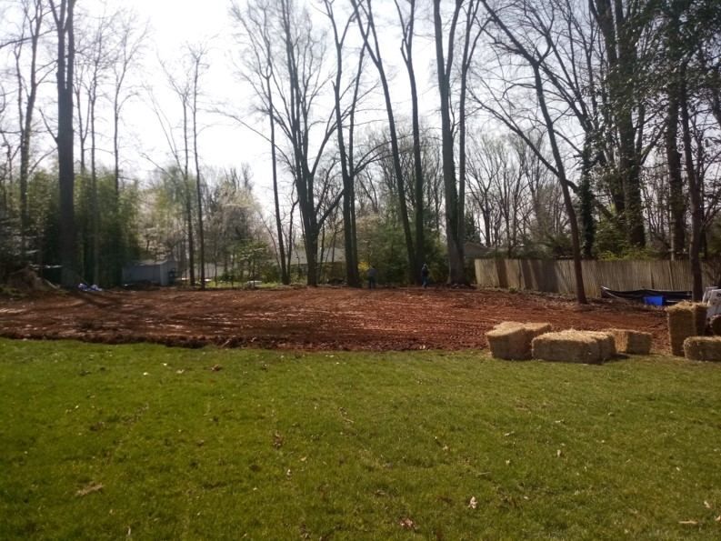 A lush green field with trees in the background and hay bales in the foreground.