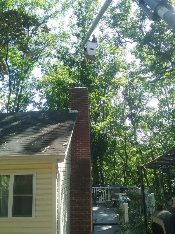 A man in a bucket is working on a chimney on top of a house.