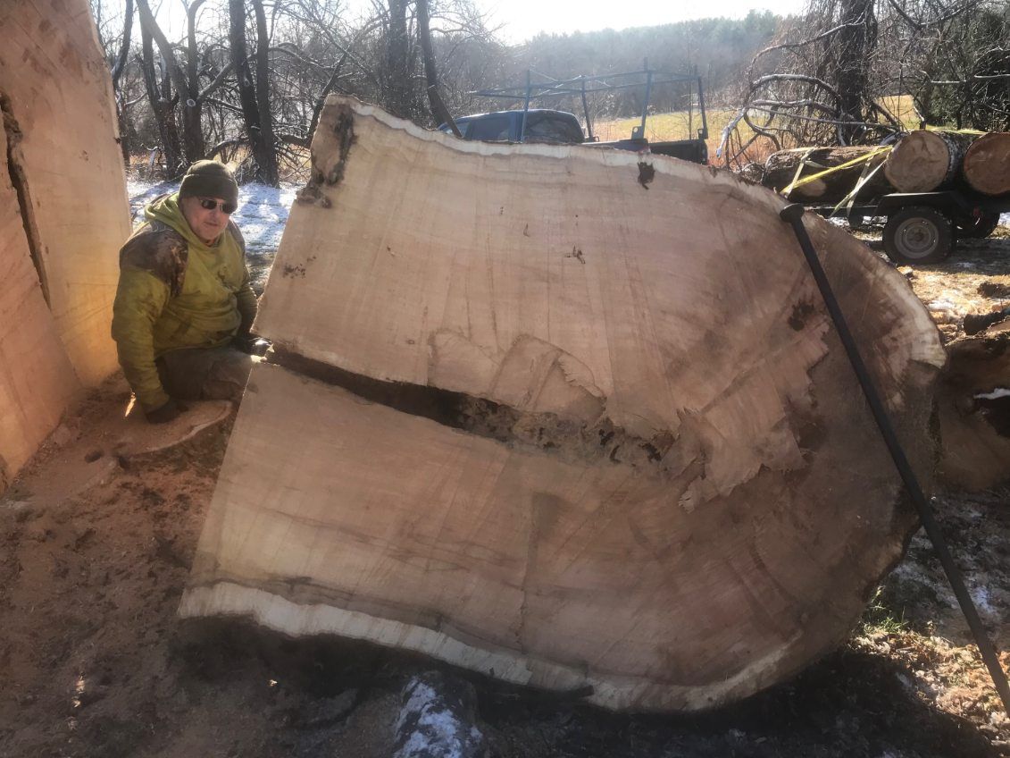 A man is sitting next to a large piece of wood.