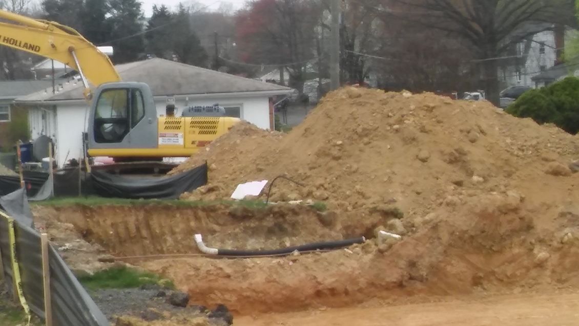A yellow excavator is digging a hole in the ground next to a pile of dirt.