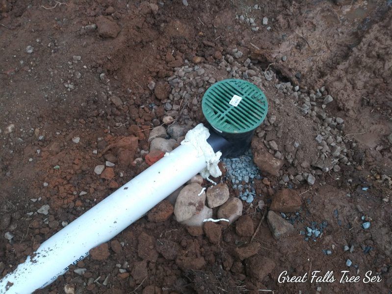 A white pipe is laying in the dirt next to a green drain