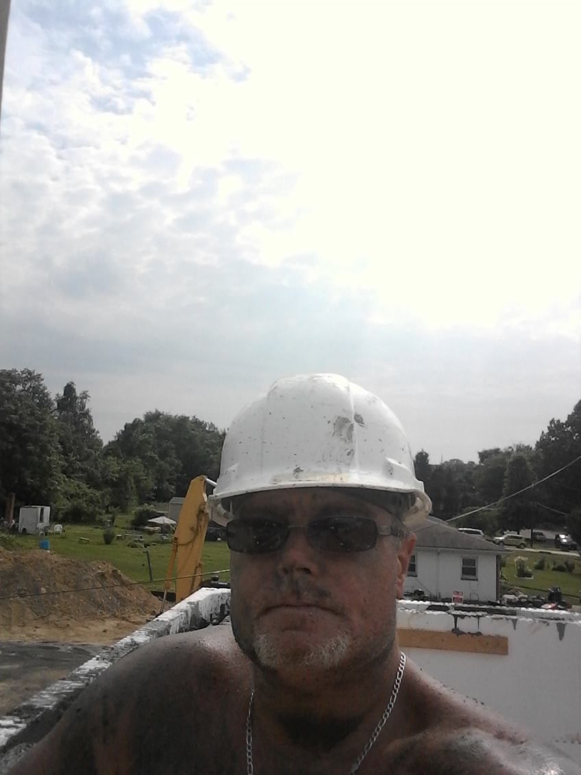 A man wearing a hard hat and sunglasses is taking a selfie.