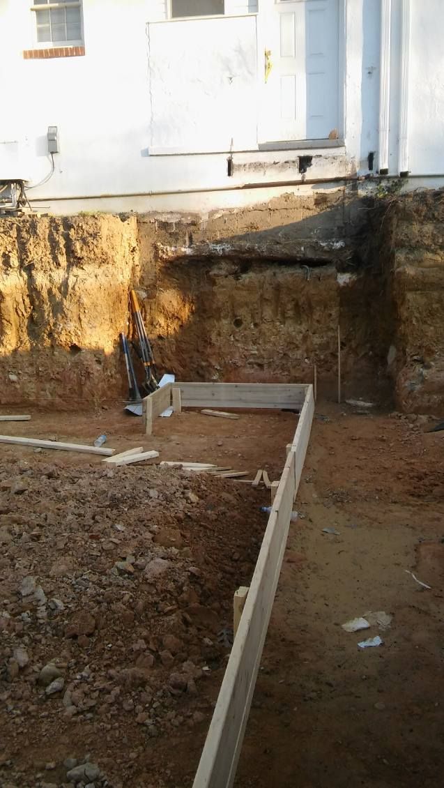 A construction site with a hole in the ground in front of a house.
