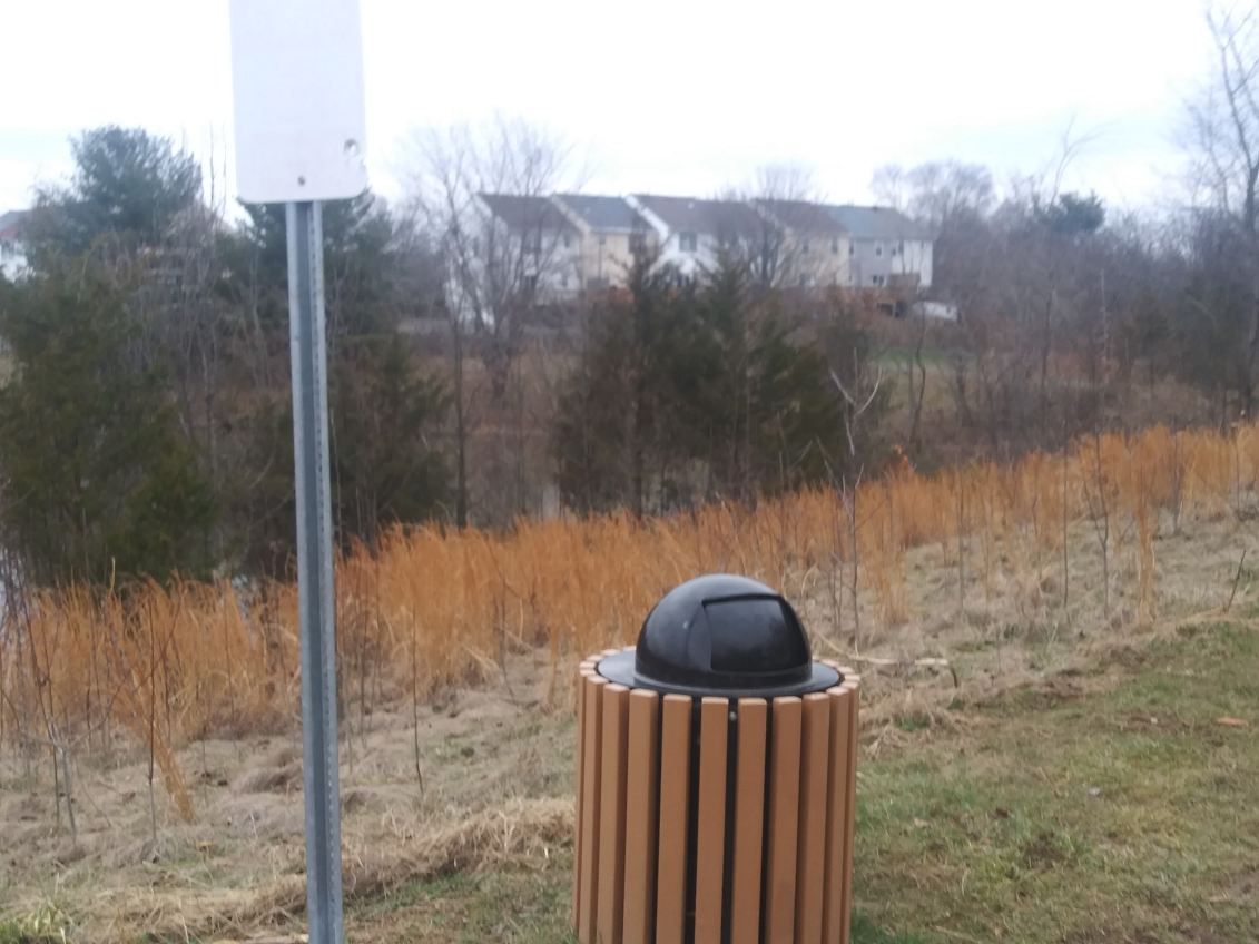 A wooden trash can is sitting in the middle of a field next to a sign.