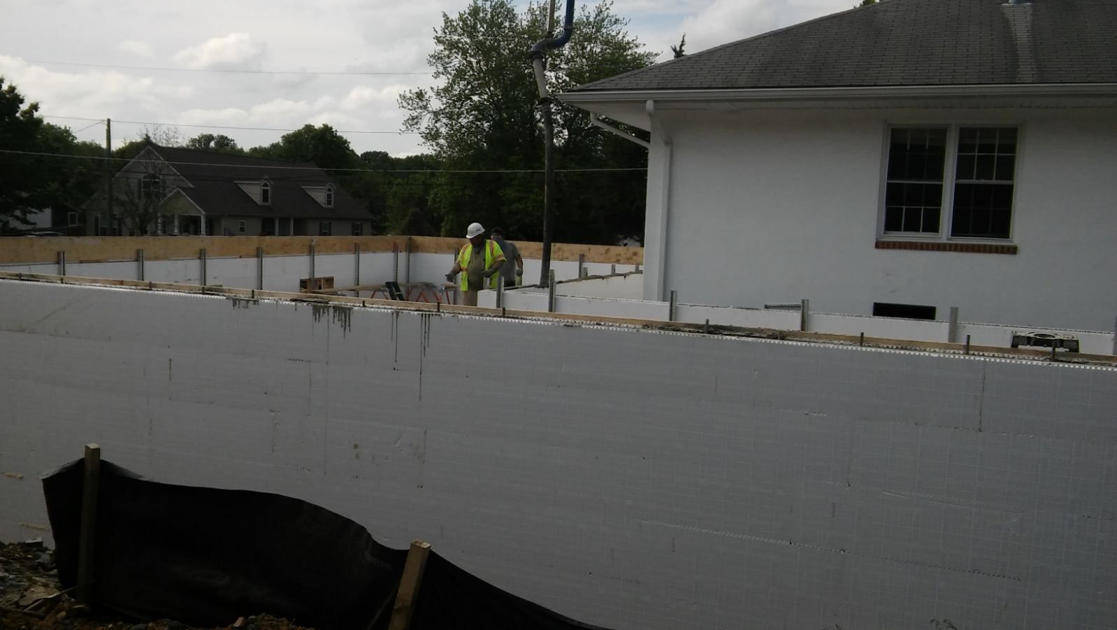 A construction worker is working on a wall in front of a white house.