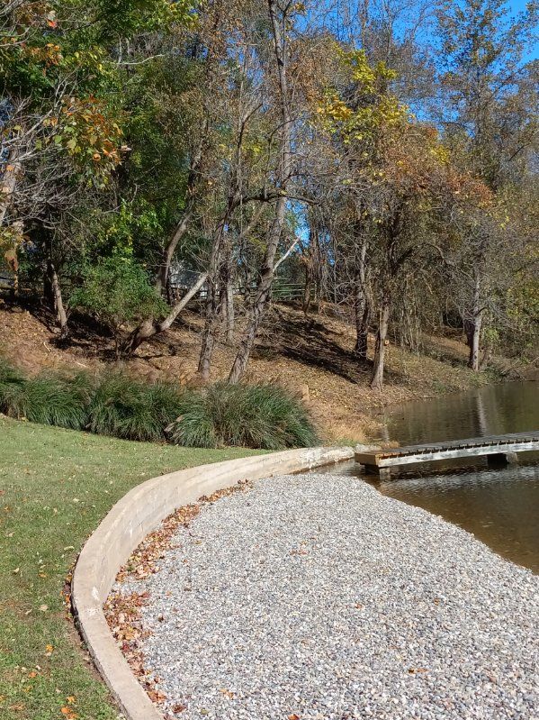 A gravel path leading to a lake with trees in the background.