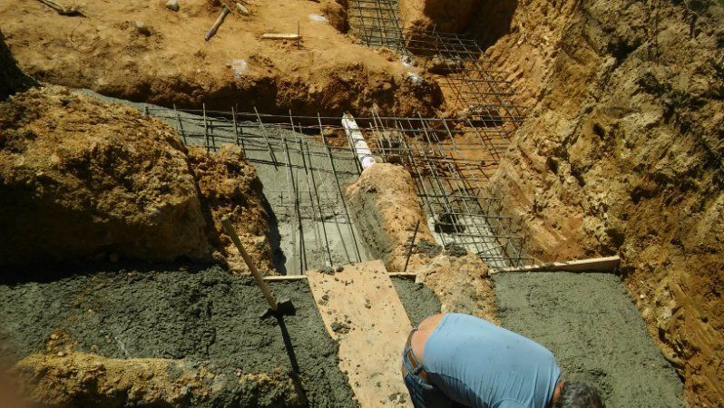 A man in a blue shirt is kneeling down in the dirt.