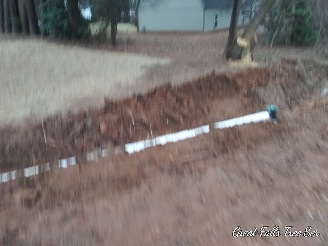 A white pipe is laying in the dirt next to a house.