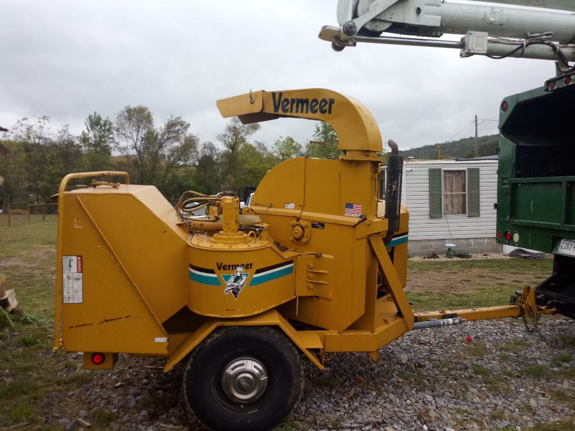 A yellow vermeer tree chipper is parked in a gravel yard