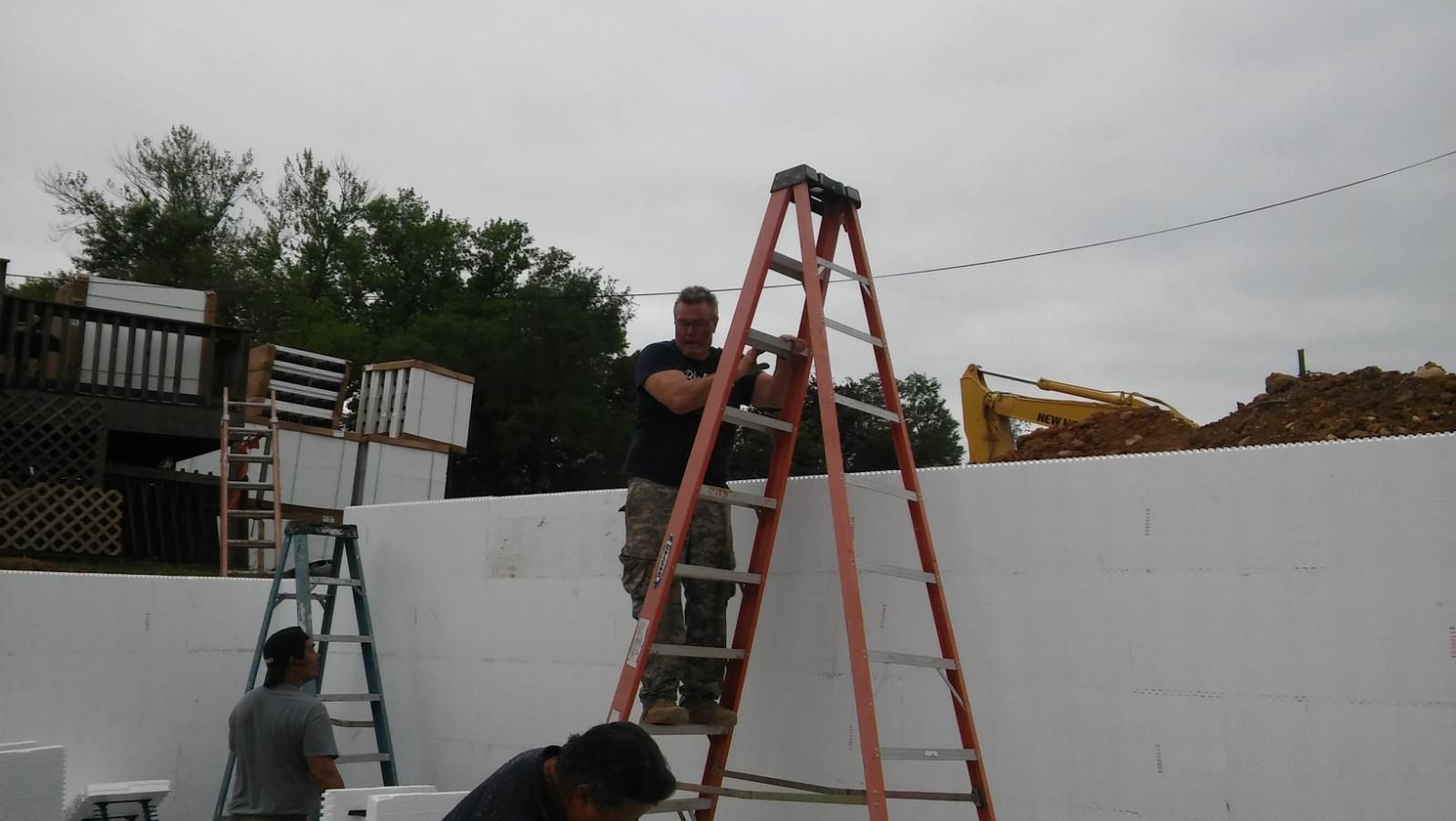 A man is standing on a ladder in front of a white wall.