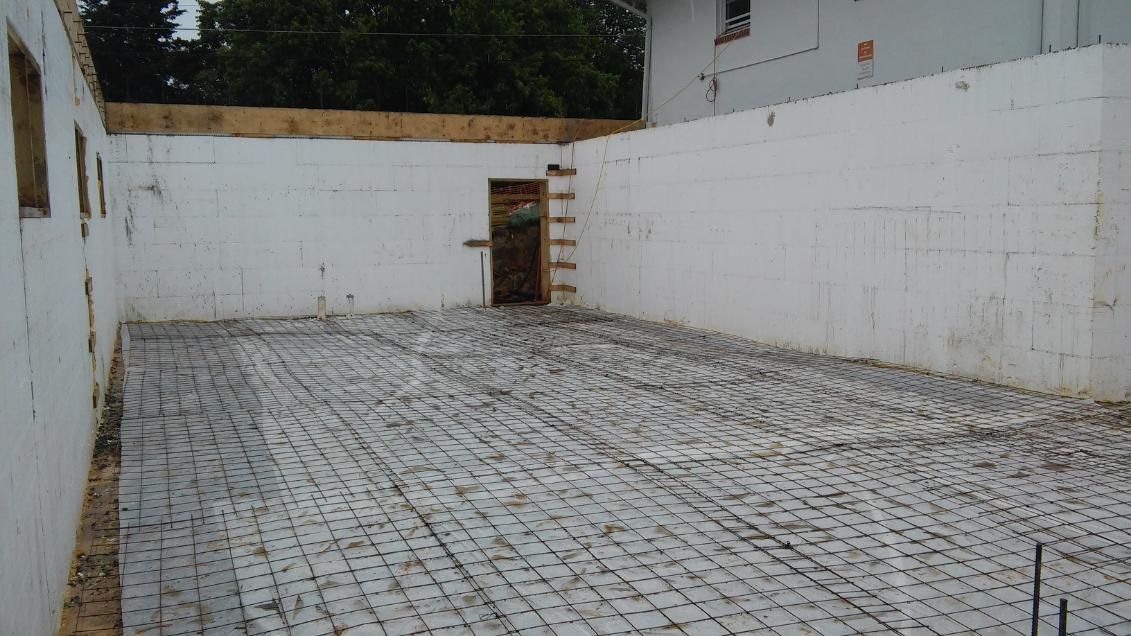 A building under construction with a concrete floor and a white wall.