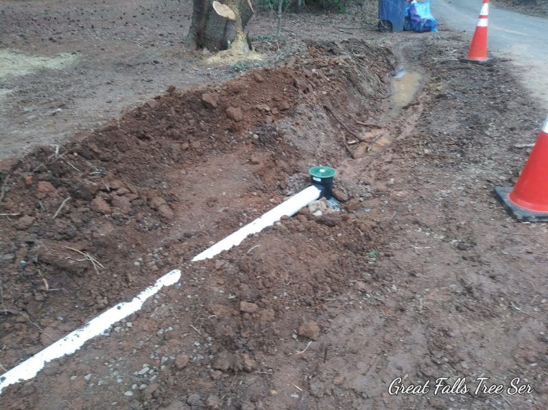 A white pipe is laying in the dirt next to a sprinkler.