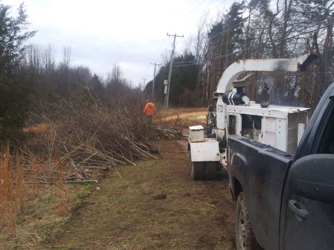 A truck is parked next to a tree chipper in a field.