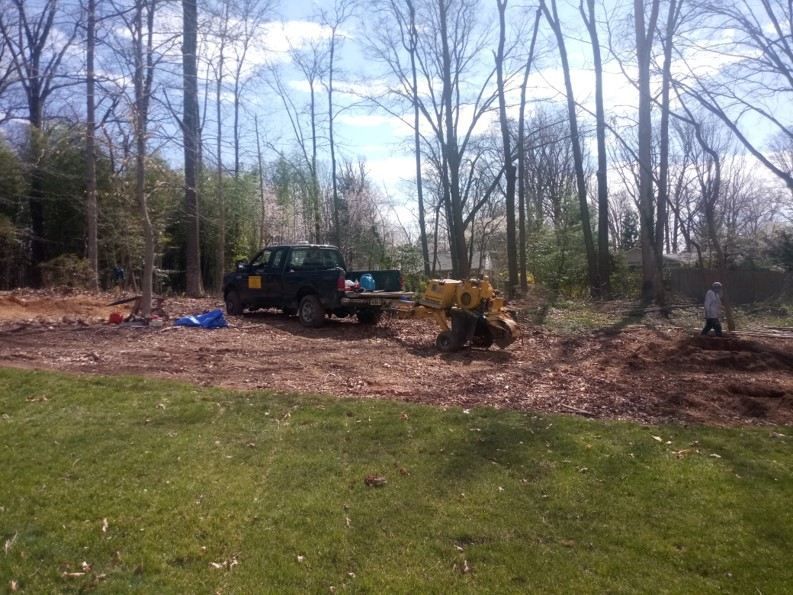 A truck is parked in the middle of a field next to a tree stump grinder.