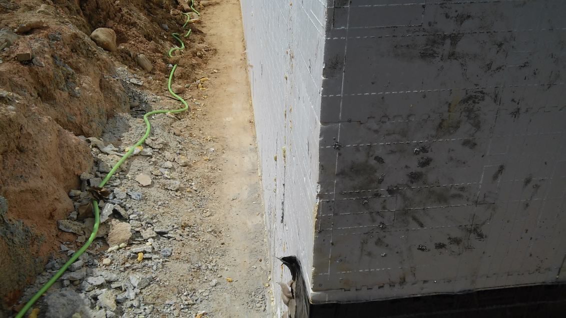A close up of a concrete wall with a green hose coming out of it.