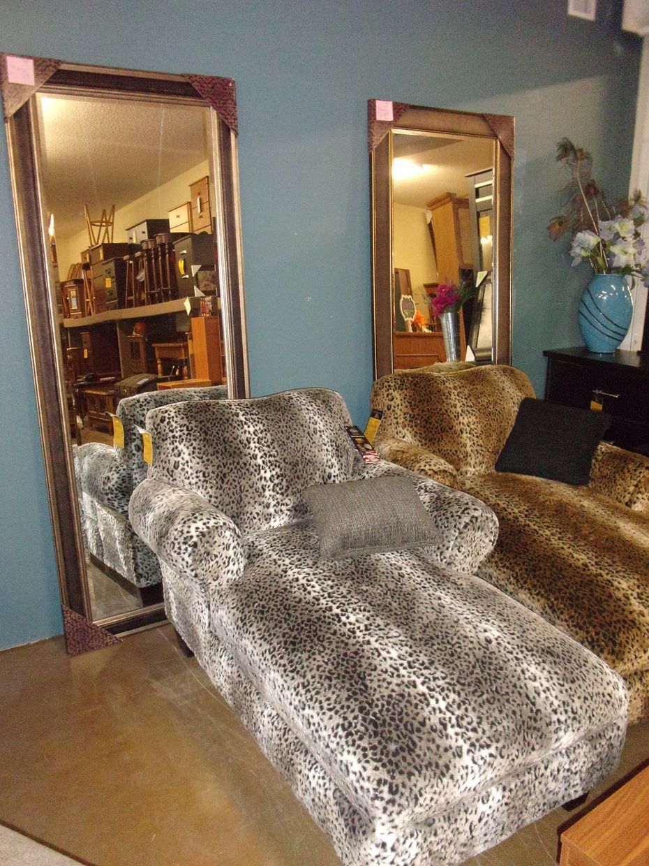 Two leopard print chaise lounges and tall framed mirrors lean against a wall.