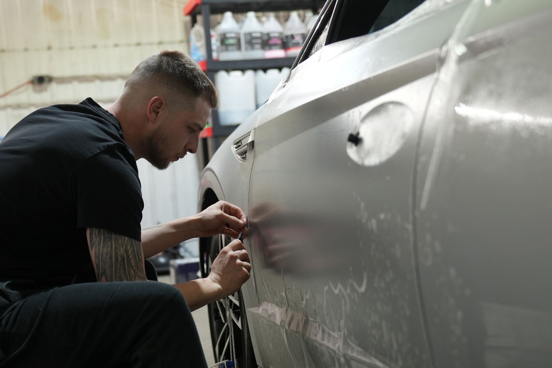 Gloved hand applying green film to a dark car panel with water droplets