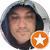 Close-up of a man in a dark cap against a teal background, with an orange star badge overlay in the corner