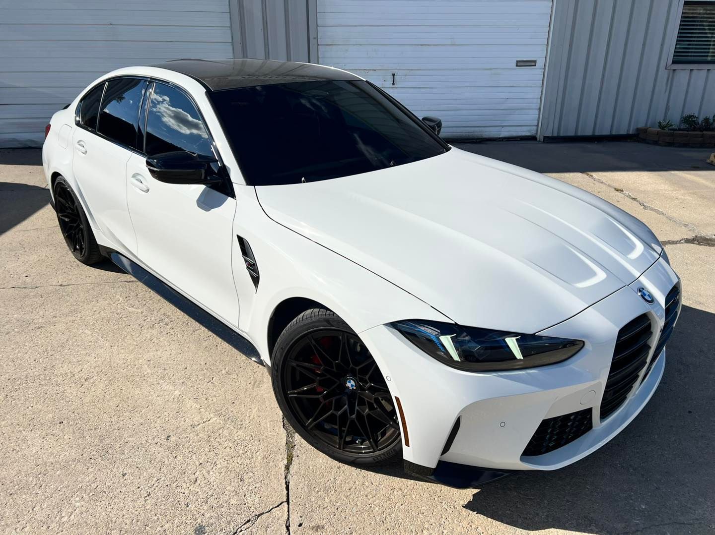 White sedan parked outside a garage, with tinted windows and black wheels.