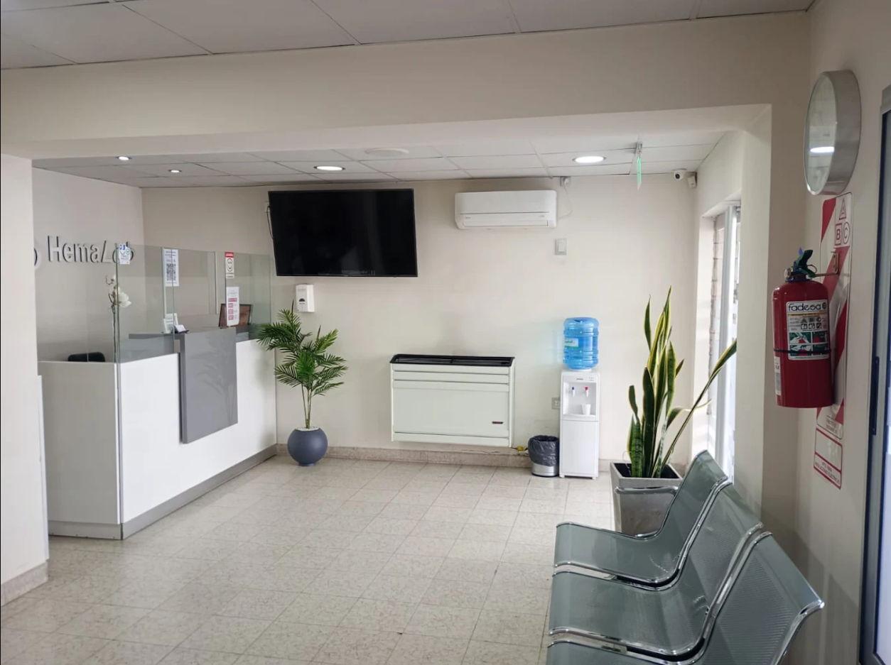 Una sala de espera con un escritorio negro, sillas y un televisor.