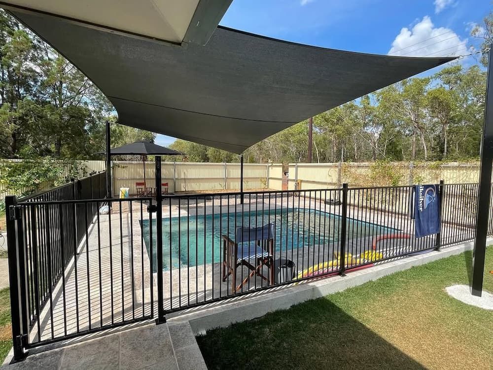 Black Fenced Pool Area With Shade Sail; Green Lawn, Trees, and Sky — Rod Hardy Plunge Pools in Girraween, NT