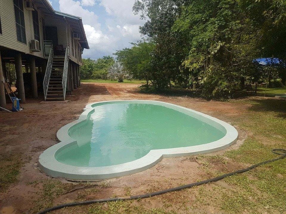 A Kidney-shaped Swimming Pool in a Yard Next to a Two-story House on Stilts — Rod Hardy Plunge Pools in Girraween, NT