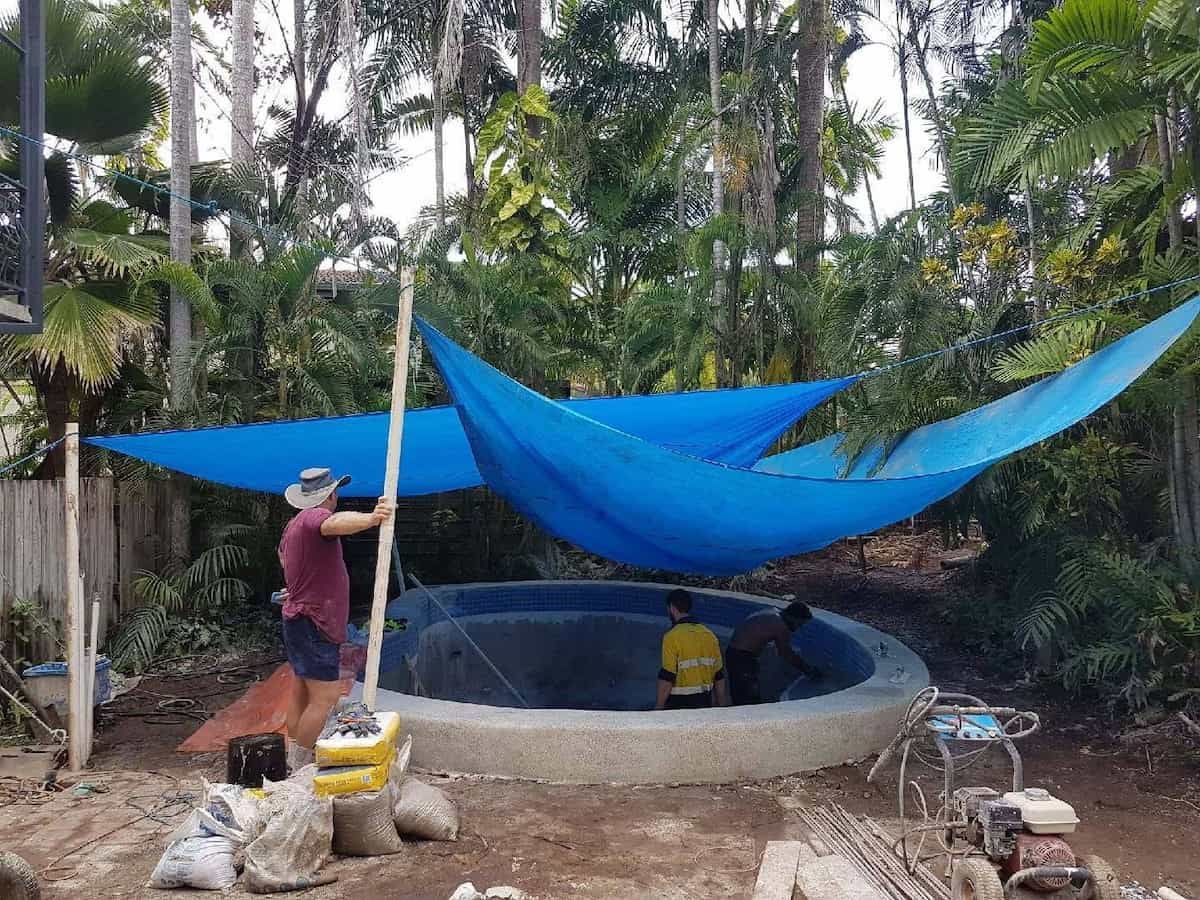 Person Adjusting Blue Shade Sails Over a Concrete Pool; Tropical Foliage — Rod Hardy Plunge Pools in Girraween, NT