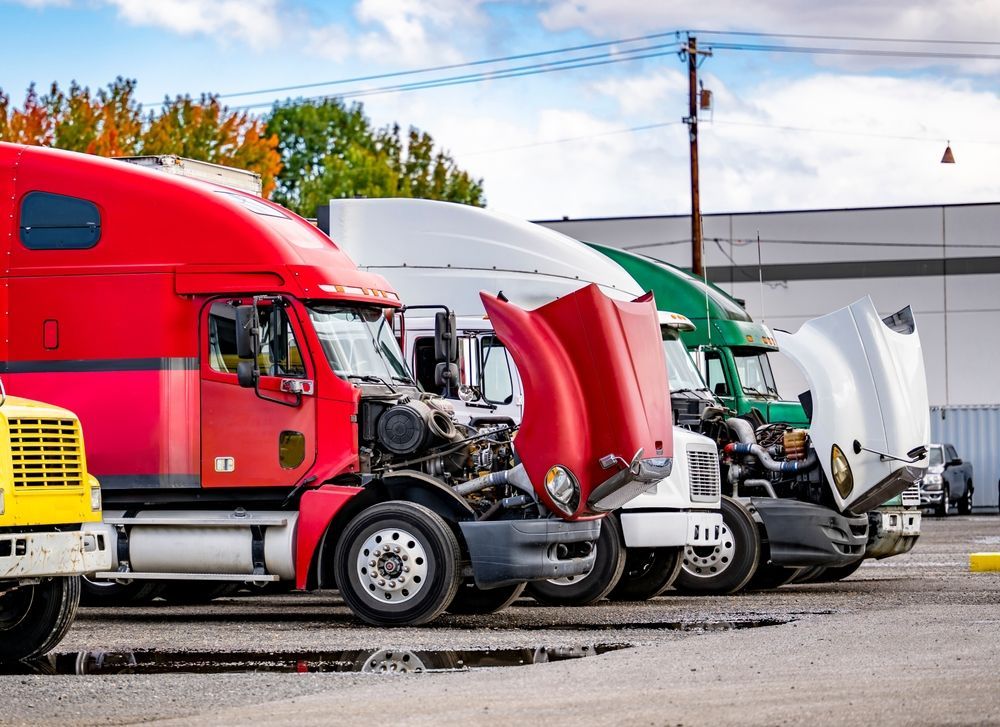 Line of parked semi trucks with open hoods in a truck lot, including red, white, and green cabs.