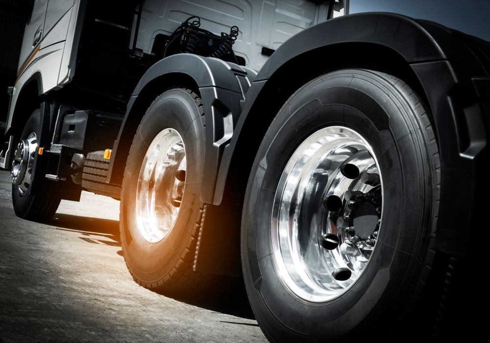 Close-up of a black semi-truck’s chrome wheels on a road, with warm sunlight reflecting off the tires