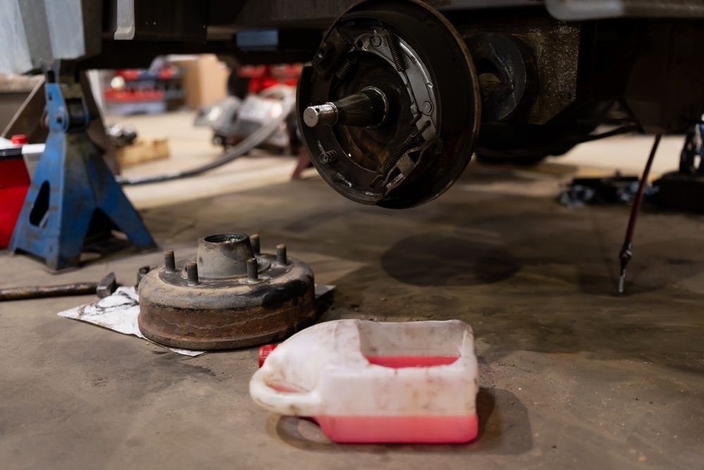 Car wheel hub and brake parts removed in a garage, with tools on the floor and a red fluid pan nearby