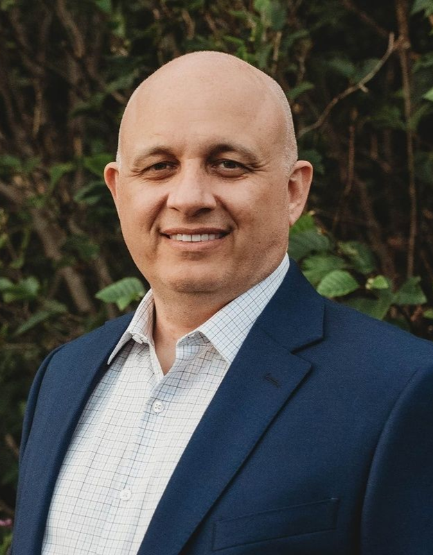 A woman with curly hair is smiling and wearing a colorful shirt.
