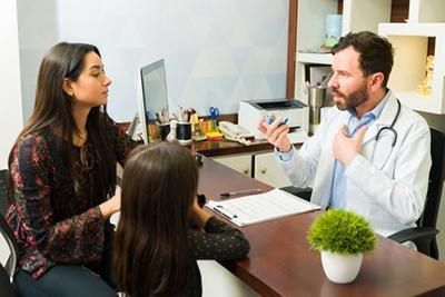 Doctor consults with a woman and child in an office setting.
