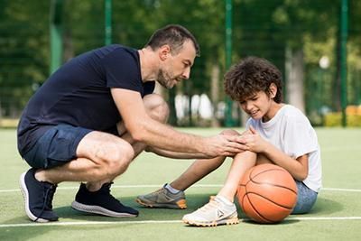 Man comforts boy with injured knee on a basketball court.